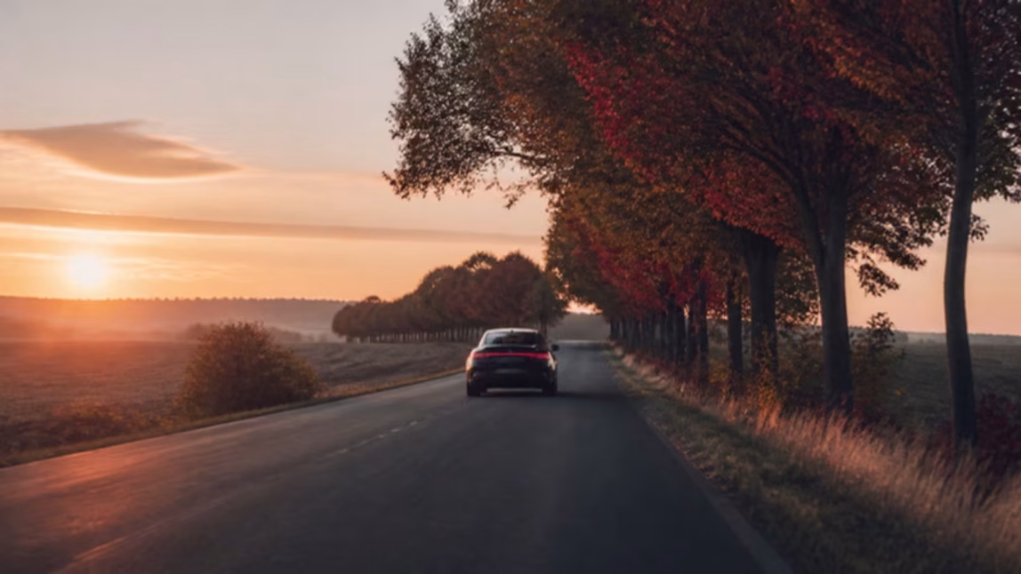 Auto na prázdné silnici mezi poli při východu slunce