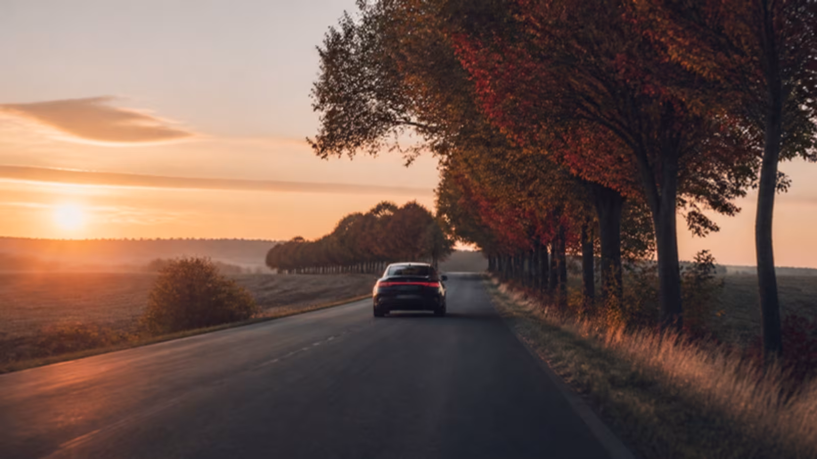 Auto na prázdné silnici mezi poli při východu slunce