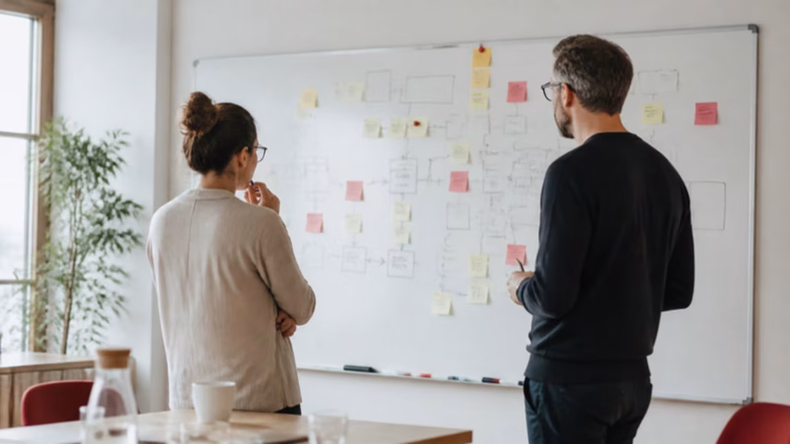 Dva lidé diskutují u tabule s diagramem procesu