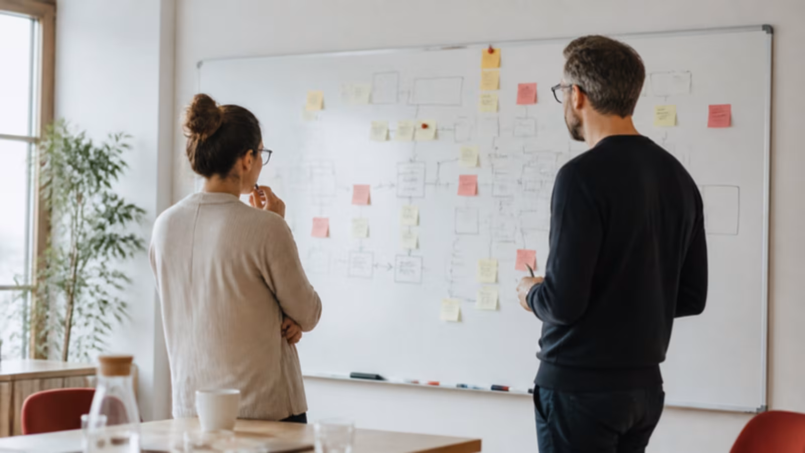 Dva lidé diskutují u tabule s diagramem procesu